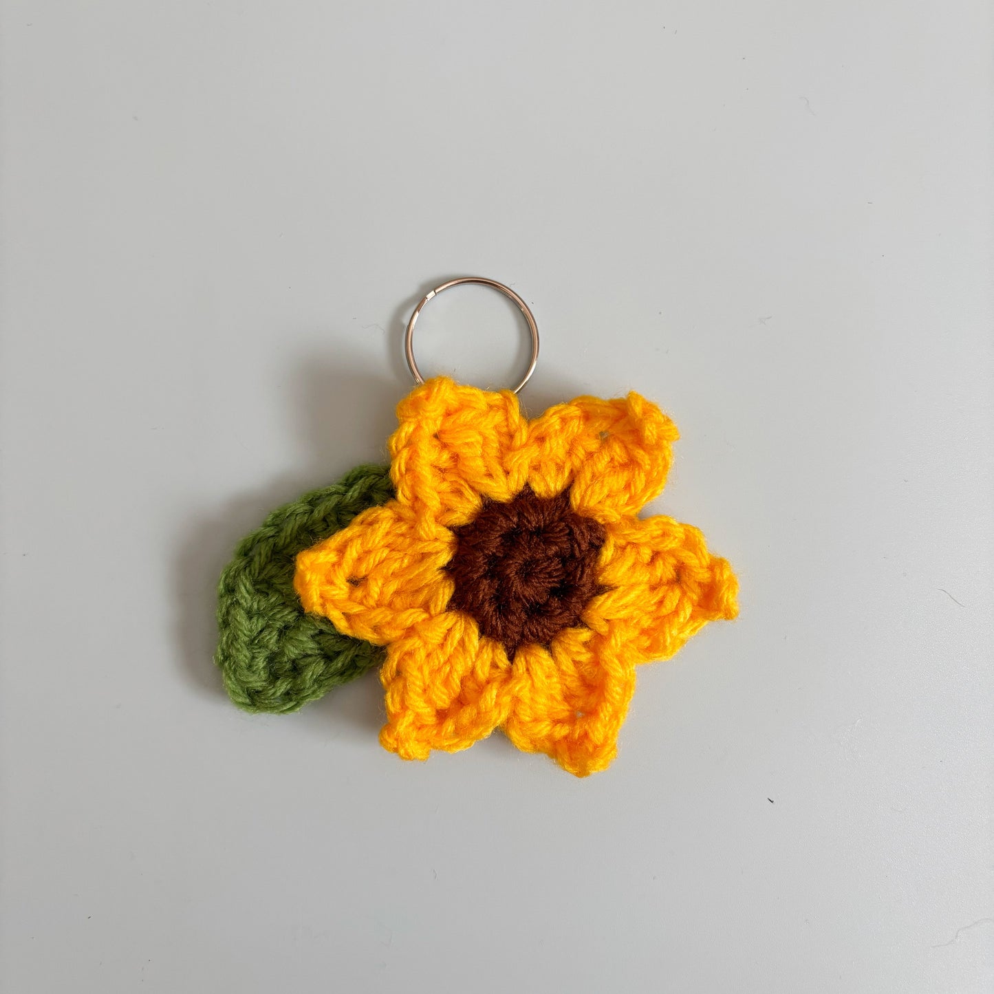 Crocheted sunflower keychain on a gray background.