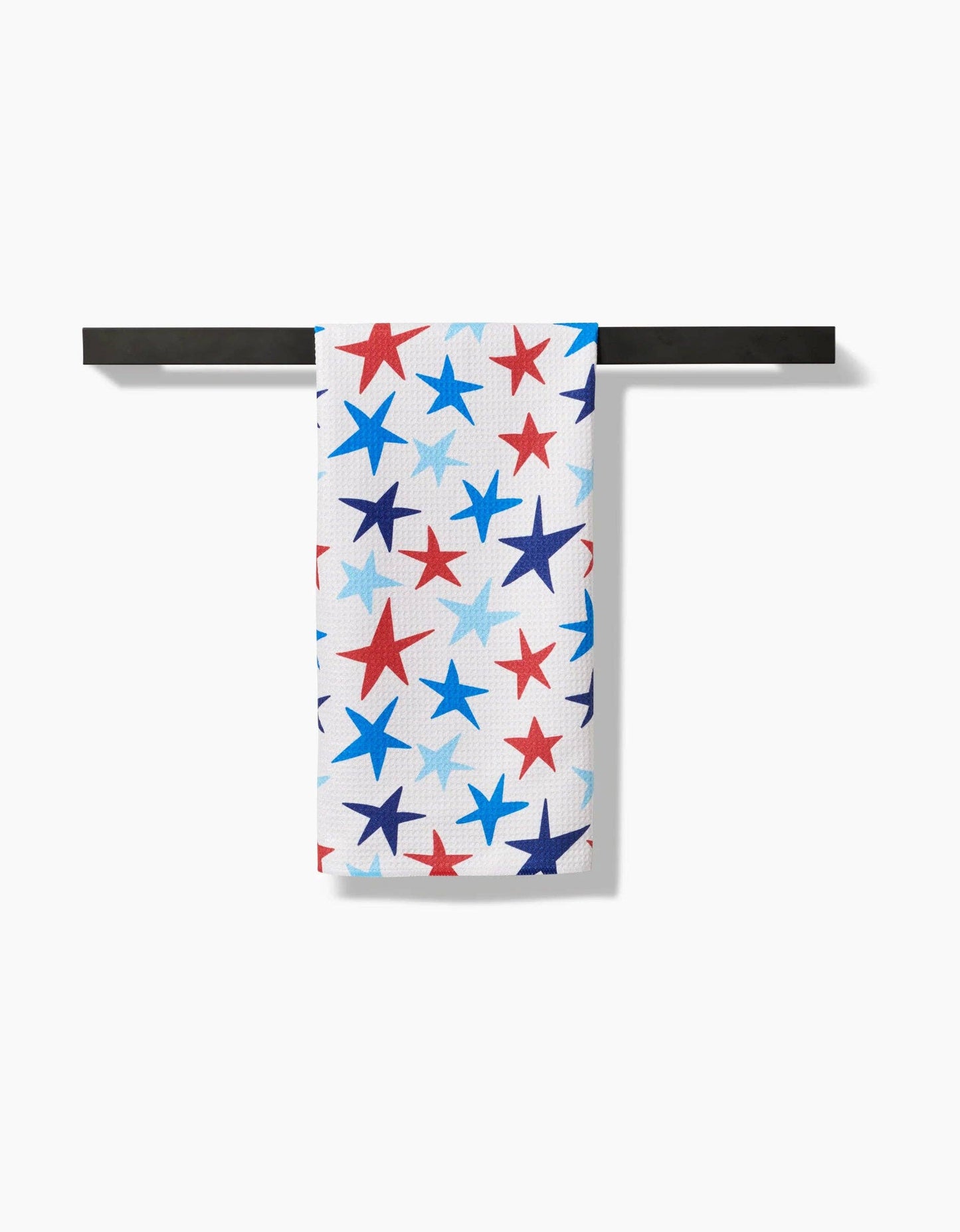 A decorative white tea towel with red, dark blue, and light blue stars of a various sizes hanging on a towel rod on a white background.