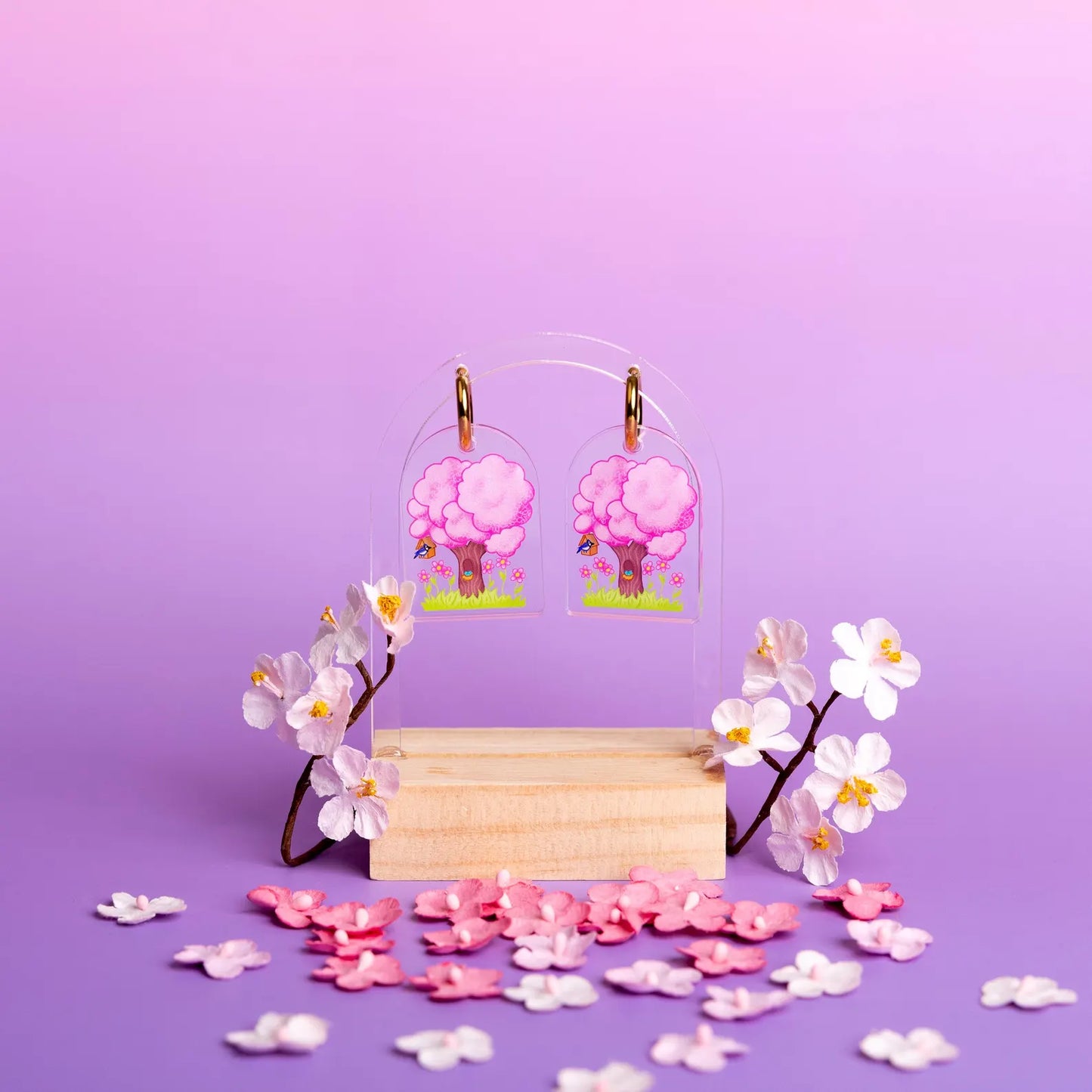 Set of spring earrings designed with a blooming pink tree. Displayed above fake pink and white flowers on a purple and light purple background