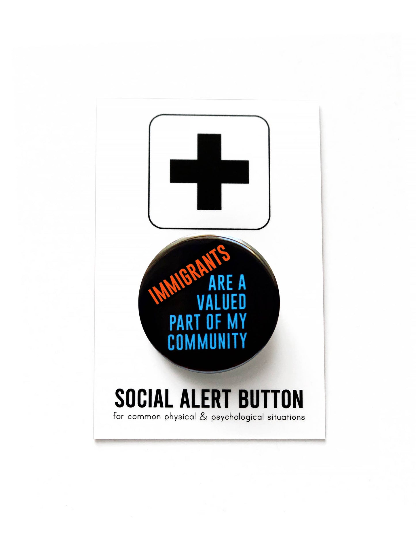 Black button with red and blue text 'Immigrants are a valued part of my community' on a black and white ‘social alert button for common physical & psychological situations’ packaging on a white background