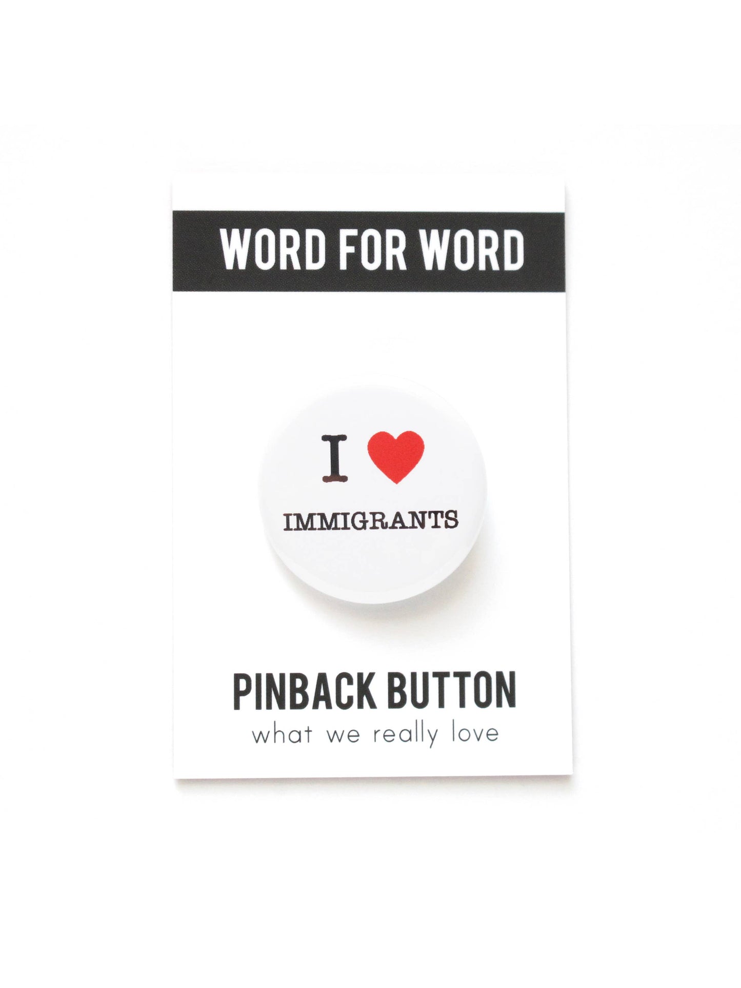 White button with “I heart Immigrants” on a black and white “Word for word, Pinback Button what we really love” packaging.