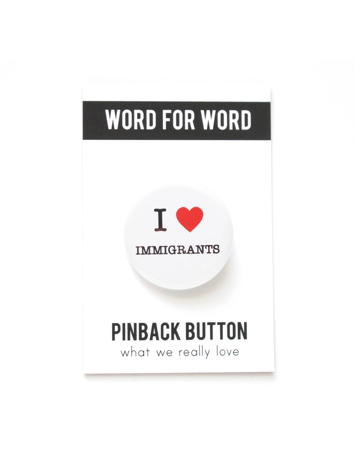 White button with “I heart Immigrants” on a black and white “Word for word, Pinback Button what we really love” packaging.