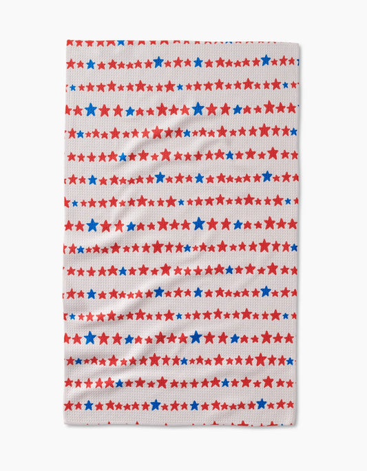 Decorative white tea towel with blue and red stars arranged in a stripe like pattern on a white background. 
