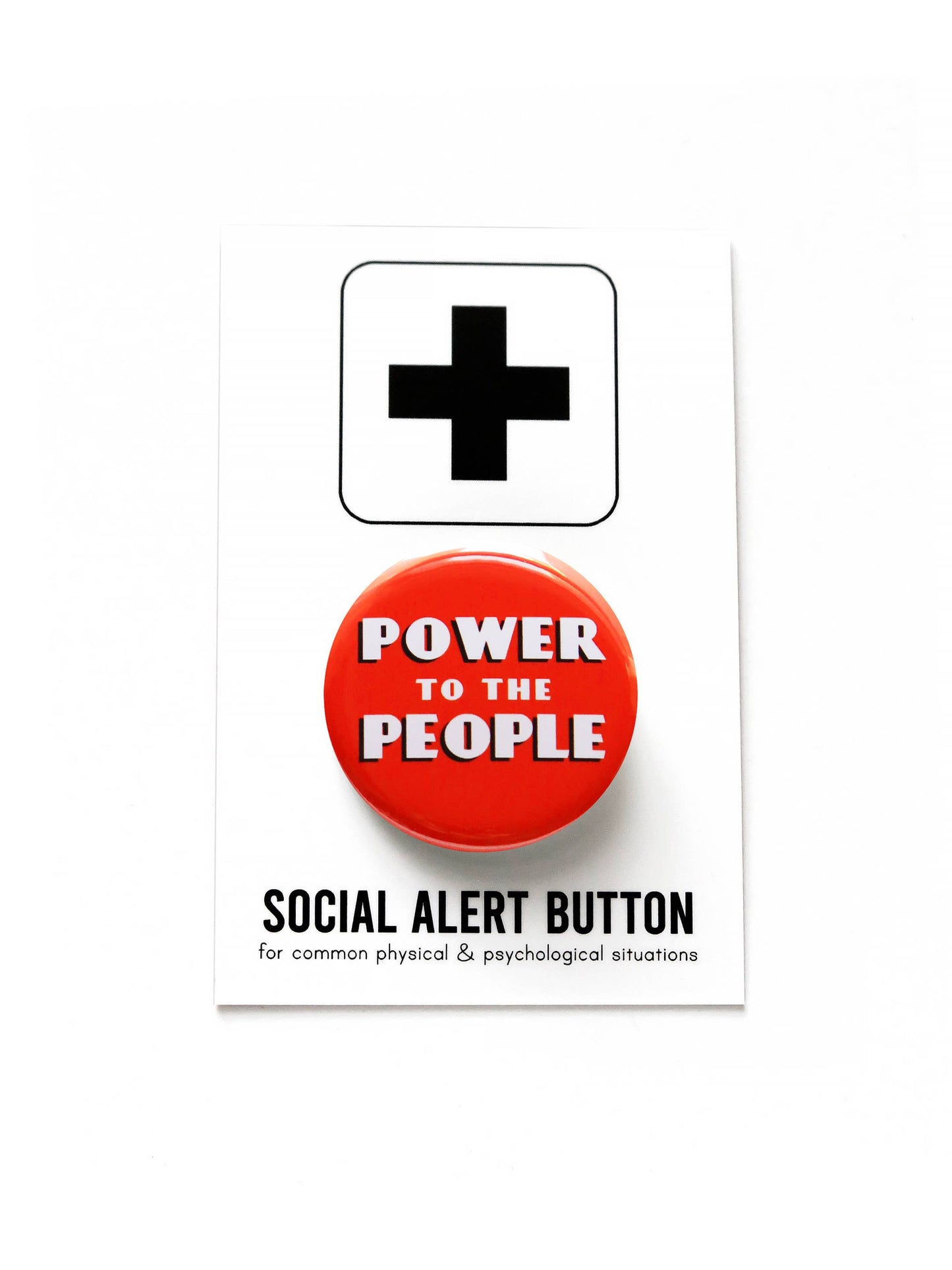 A red button with white text stating ‘Power to the people’ on black and white ‘Social alert button, for common physical & psychological situations’ packaging on a white background.
