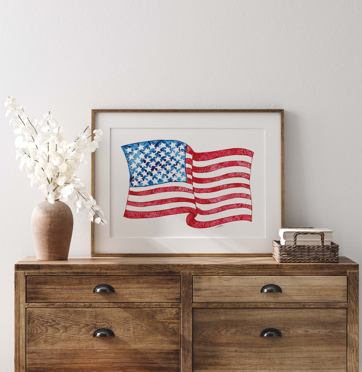 Framed American flag print on a wooden dresser with decorative items.
