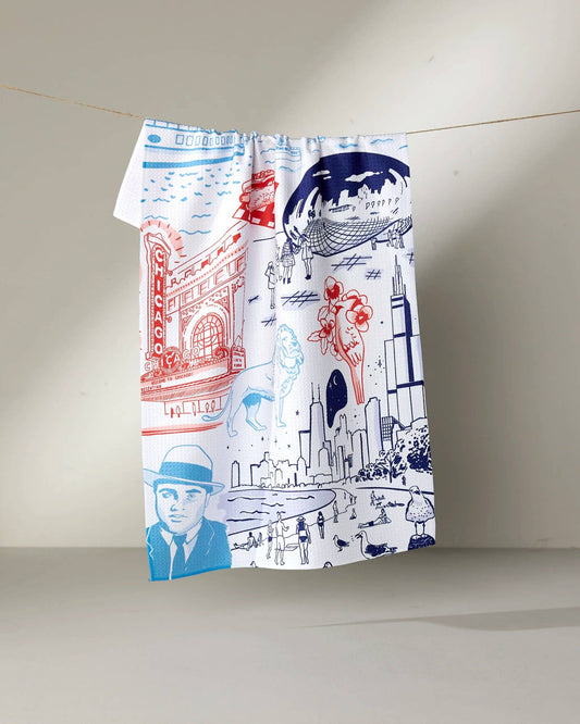 Decorative tea towel of Chicago landmarks, famous figures, plants, and animals. On a beige background hanging from a line.