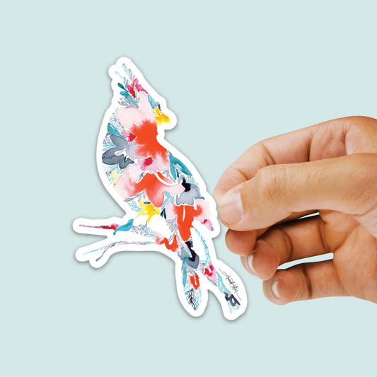 Hand holding a colorful bird-shaped sticker against a light blue background.