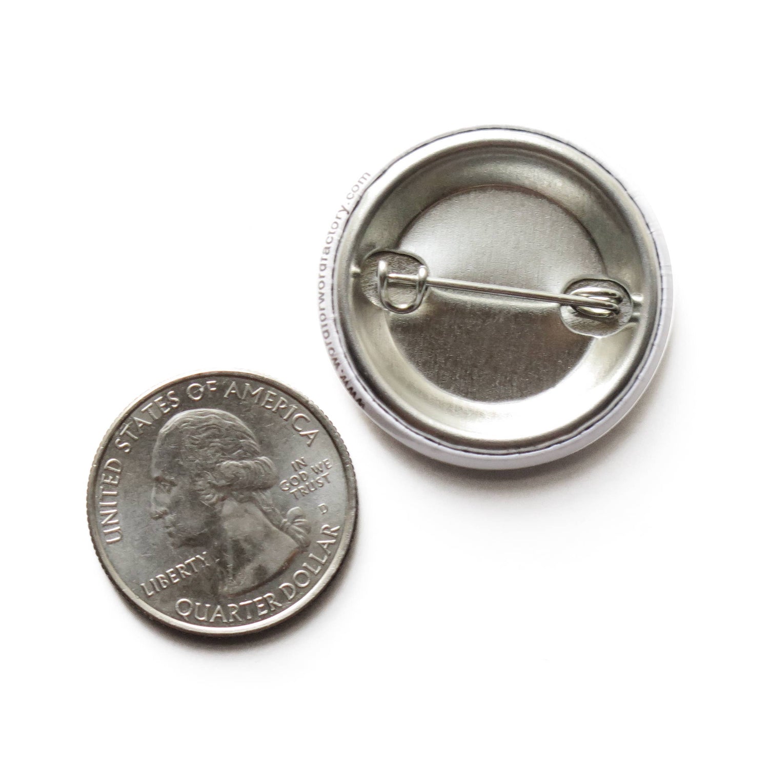 US quarter coin next to the back of a button with metal pin showing size comparison on white background. 