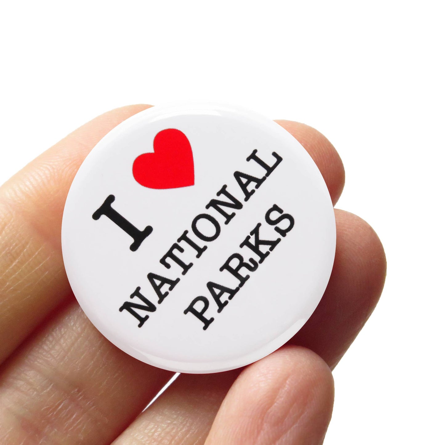 White button badge with ‘I heart national parks’ held by hand against a white background. 