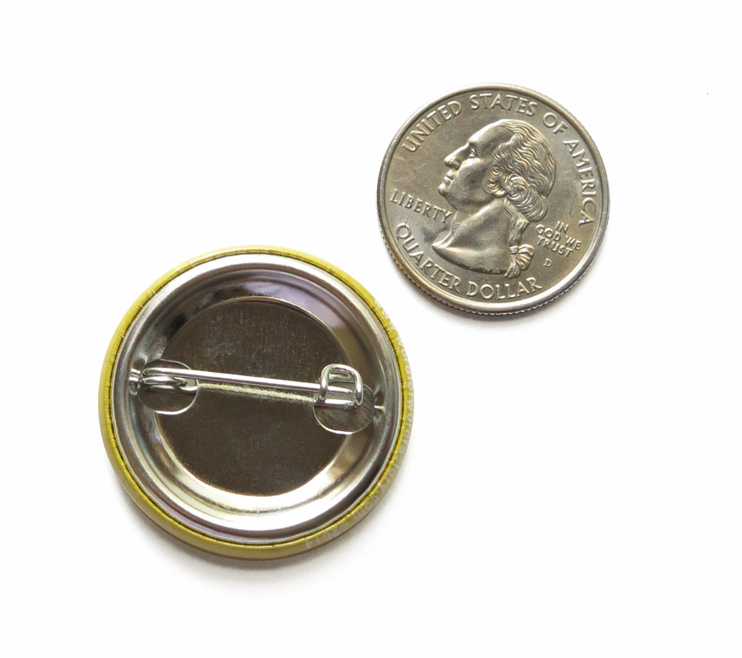 Back of button with metal pin next to a US quarter coin showing size comparison on top of a white background. 