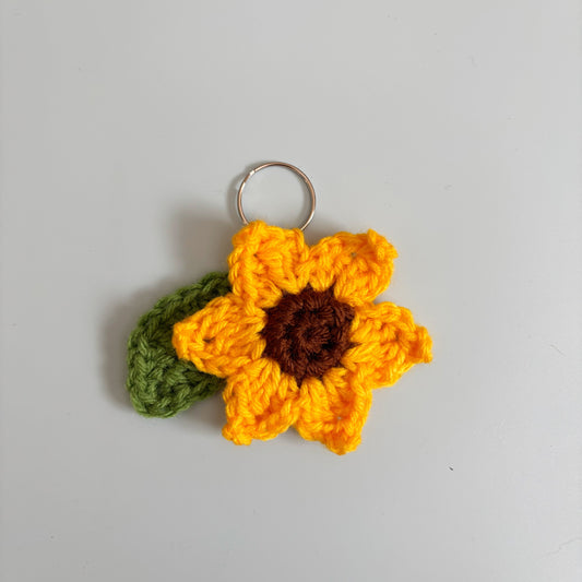 Crocheted sunflower keychain on a gray background.