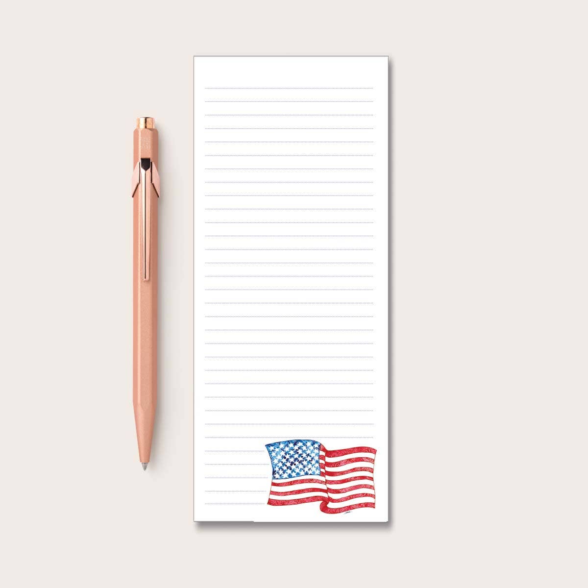 Notepad with American flag design at the bottom and a rose gold pen on a light gray background