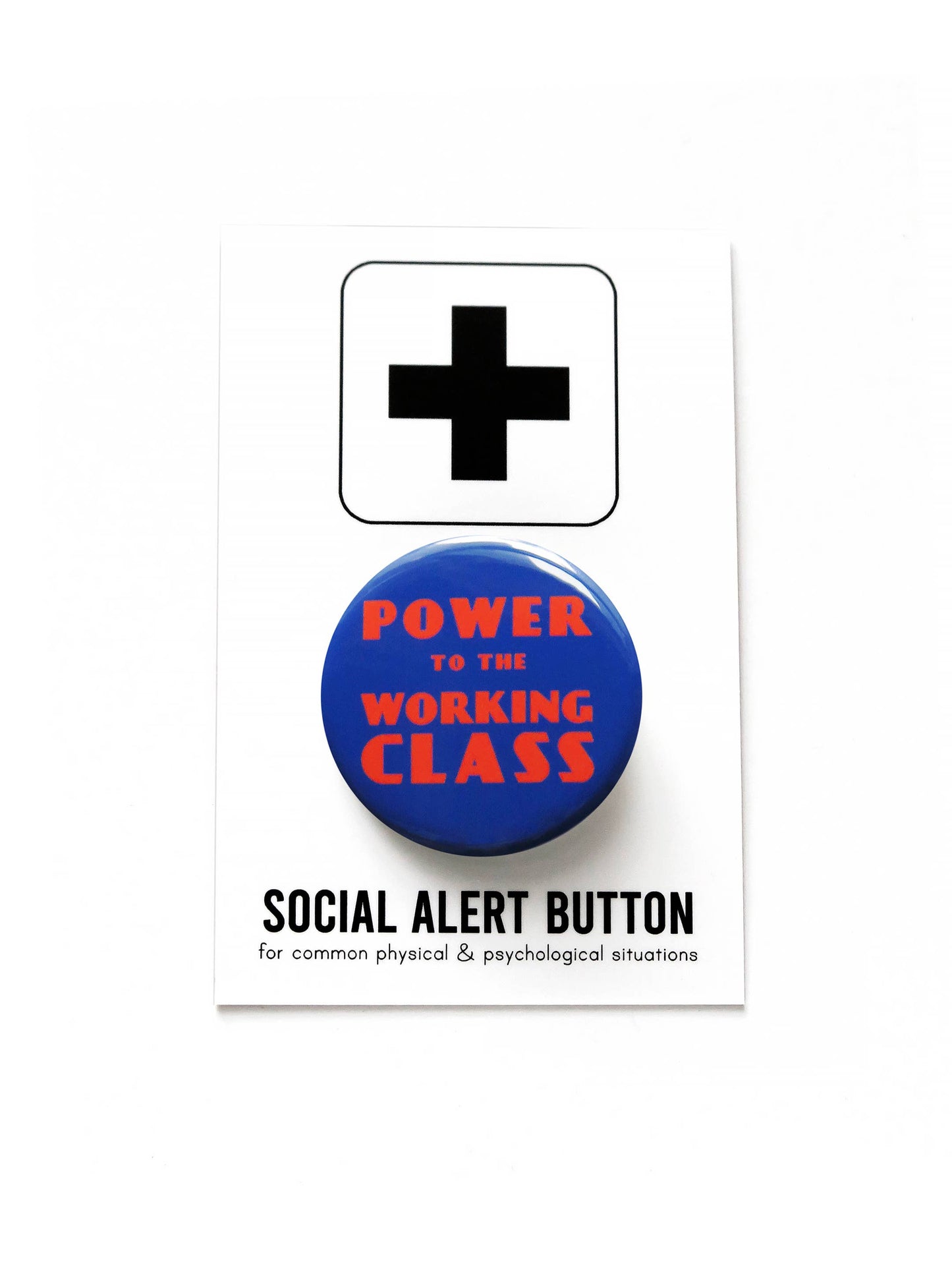 Blue button with red 'Power to the Working Class' text on black and white ‘Social alert button, for common physical & psychological situations’ packaging. On top of a white background.