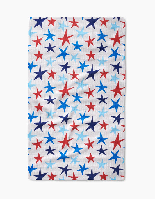 A decorative white tea towel with red, dark blue, and light blue stars of various sizes on a white background. 