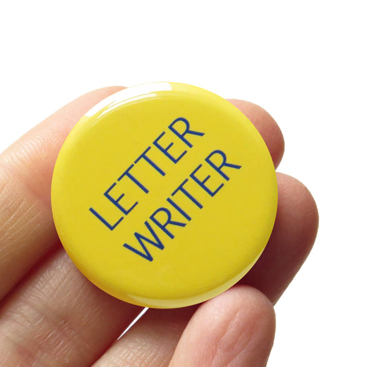 Yellow button with 'Letter Writer' text held in a hand against a white background