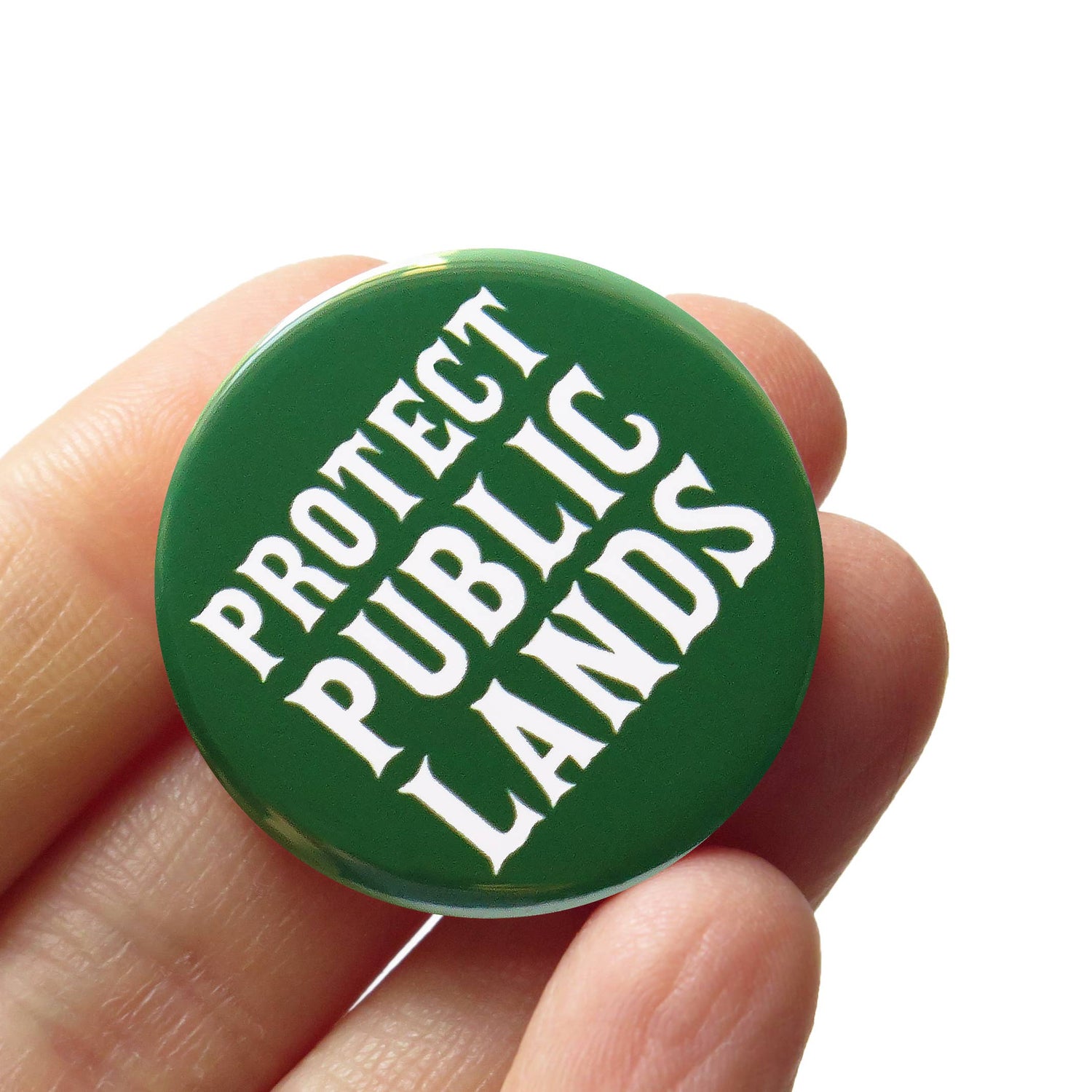 Green button with 'Protect Public Lands' text held by a hand against a white background. 