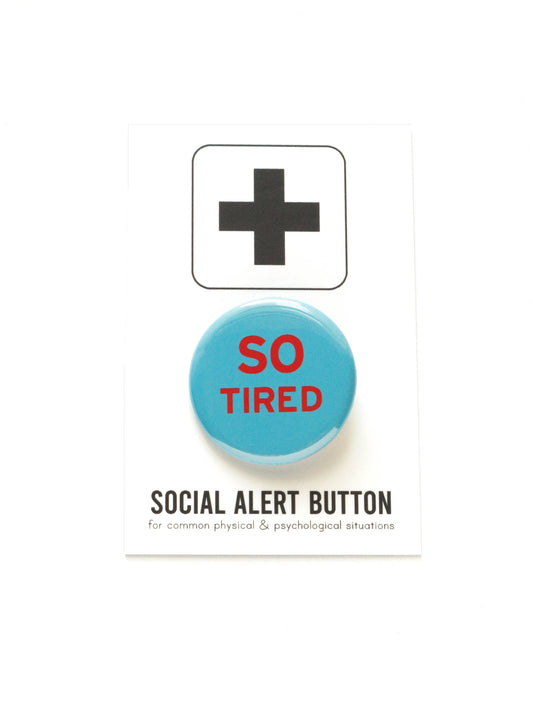 Blue button with red text ‘So tired’ on a black and white ‘Social alert button for common physical & psychological situations’ packaging.