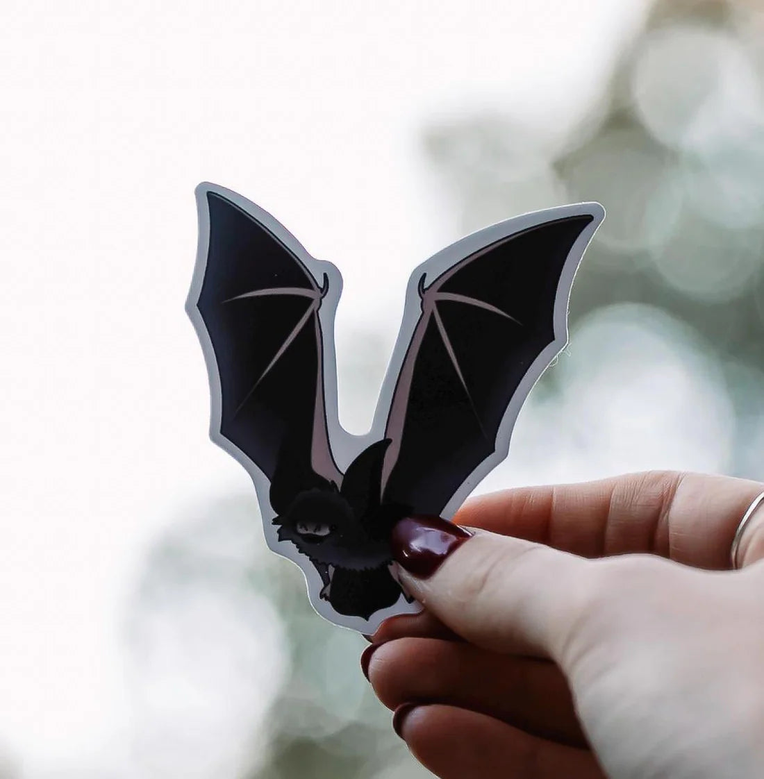 Hand holding a bat-shaped sticker against a blurred natural background