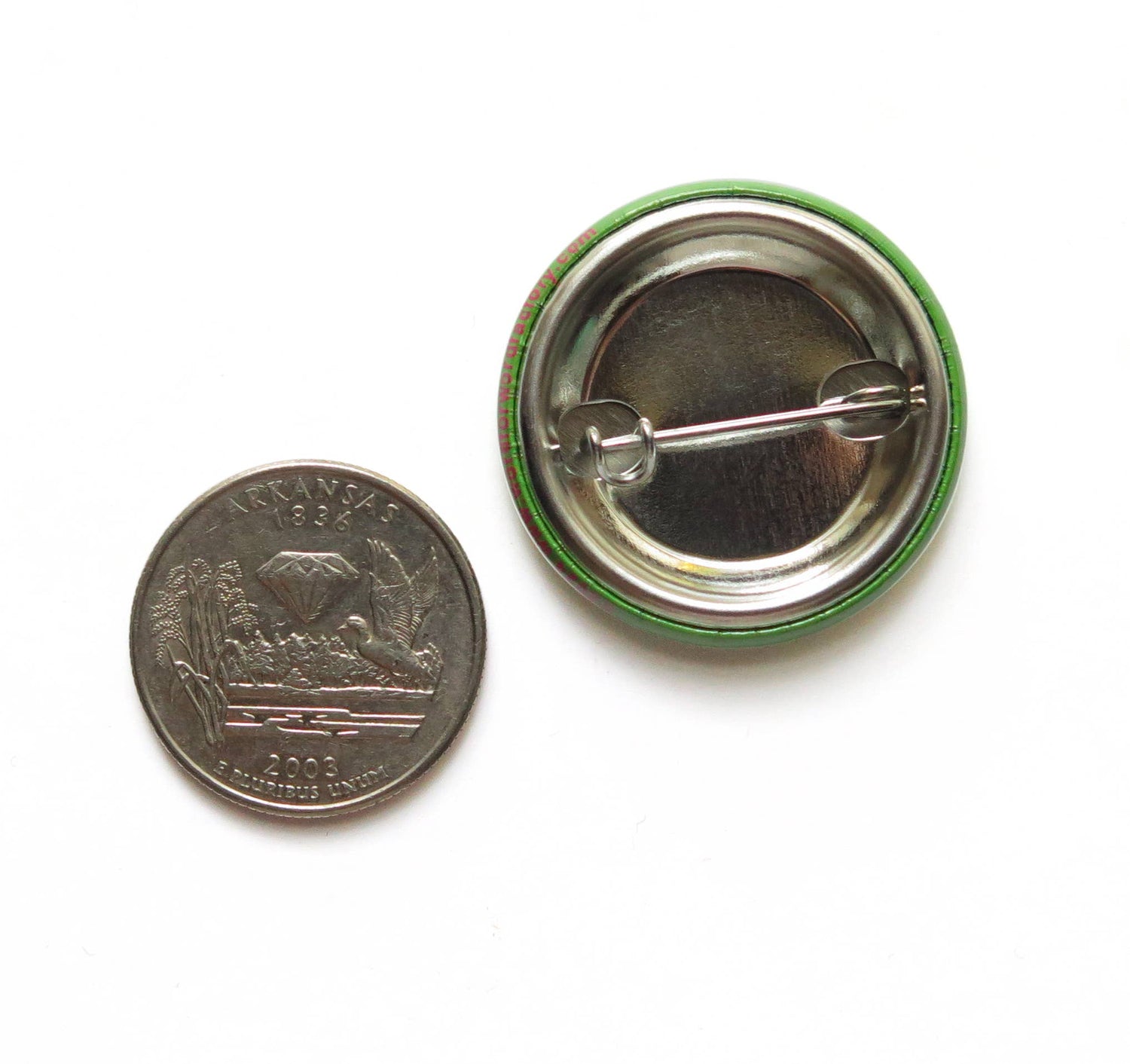 US quarter coin next to the back of a button with a metal pin showing size comparison on a white background.