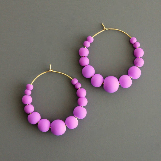 A pair of purple glass hoop earrings with gold plating on a textured background.