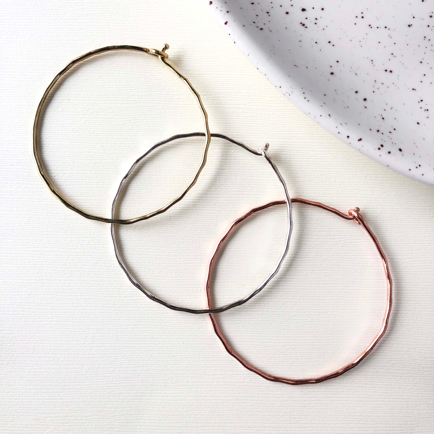 Product photo of the gold, silver, and copper “Interlocking Ripple” Bracelets, next to each other.