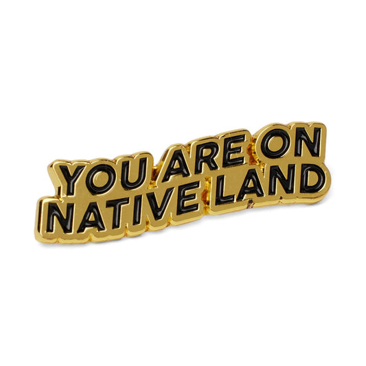 Image of the gold Native Land Era Pin, reading “You Are On Native Land”.