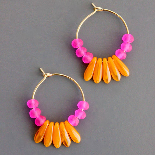 A pair of gold-plated brass hoop earrings with matte pink glass and orange glass accents, displayed against a grey background.