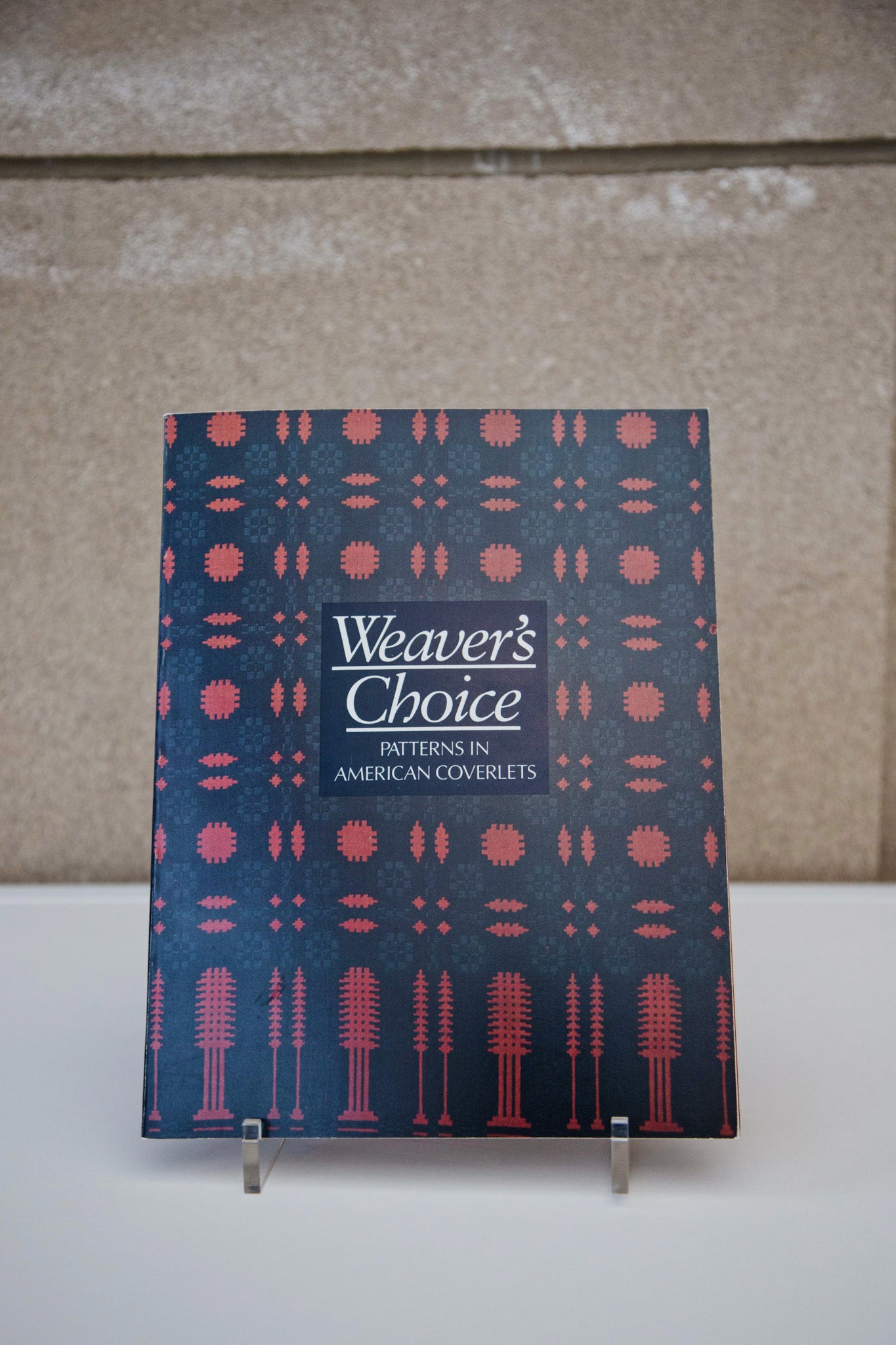 “Weavers Choice: Patterns in American Coverlets” book on a book stand.