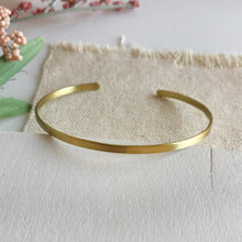 Load image into Gallery viewer, Styled photo of the gold “Simple Band” Cuff.
