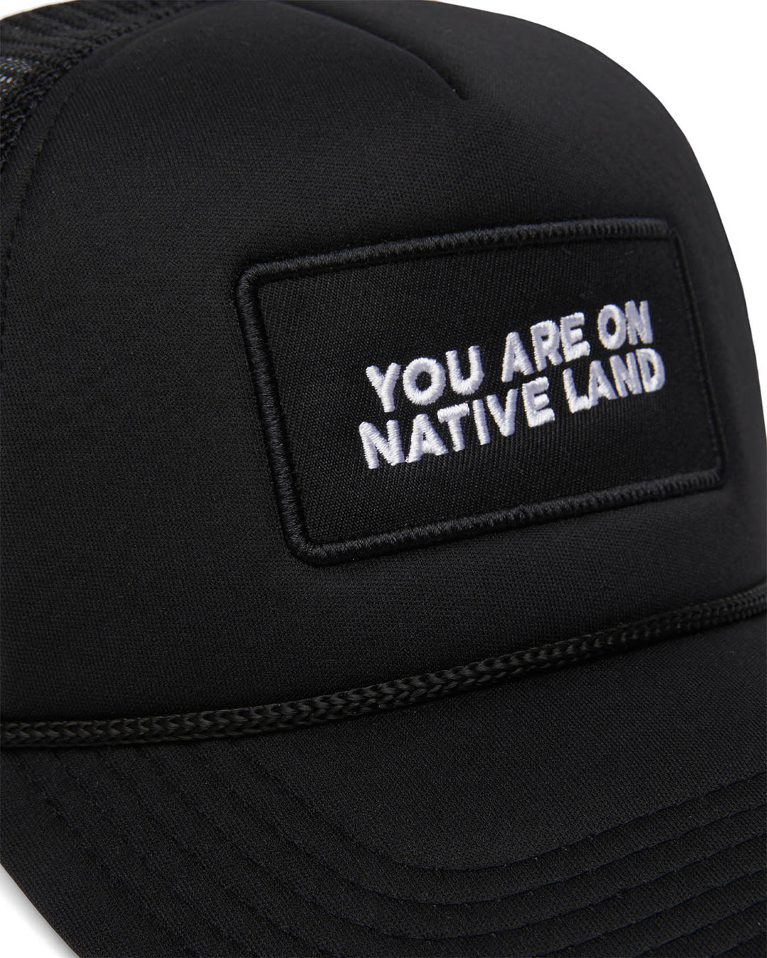 Detail photo of “You Are On Native Land” trucker hat in black embroidery.