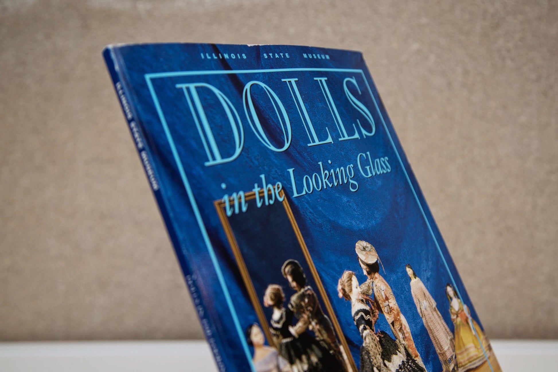 Close up image of the top of the front cover of the book “Dolls in the Looking Glass: The Joy E. Orozco Collection”.